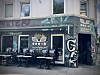 Geschlossenes Café mit „Torrefaktum“-Logo, leeren Tischen und Stühlen sowie Graffiti an der Fassade.