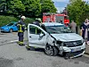 Stark beschädigter Kleinwagen auf der Straße, Feuerwehrleute und Passanten daneben