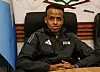 Mann in schwarzer FIFA-Jacke sitzt an einem Tisch vor Flagge und Emblem in einem Raum.