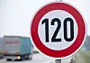 Verkehrsschild mit Tempo 120 an einer Autobahn, dahinter ein vorbeifahrender Lastwagen.
