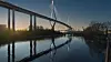 Moderne Köhlbrandbrücke bei Sonnenuntergang mit Spiegelung im ruhigen Wasser.