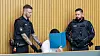Angeklagter verbirgt im Lübecker Gerichtssaal sein Gesicht, flankiert von zwei Polizeibeamten.