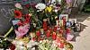 Blumen, Kerzen und gerahmte Fotos als Gedenkaltar vor einem Zaun.