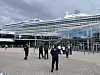 Kreuzfahrtschiff am Terminal, davor mehrere Personen auf dem Vorplatz.