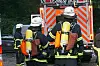 Zwei Feuerwehrleute mit Atemschutz vor einem Löschfahrzeug mit offenem Heck.