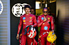 Lewis Hamilton neben Charles Leclerc, beide in Rennkleidung und mit Helm in der Hand.