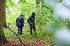 Polizeibeamte untersuchen mit einem Metalldetektor den in Planquadrate aufgeteilten Waldboden.