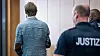 Christian B. steht mit dem Rücken zur Kamera, links sind zwei Justizbeamte