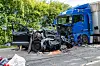 Zerstörter Pkw neben blauem Lkw auf der Straße, Trümmer und ausgelaufene Flüssigkeit auf der Fahrbahn.