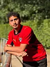 Junger Fußballer im roten Puma-Trikot lehnt an einem Geländer im Freien.