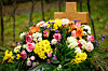 Farbenfrohes Blumenarrangement auf einem Grab mit Holzkreuz im Hintergrund.