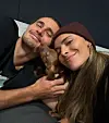 Alexander Zverev und Sophia Thomalla kuscheln mit kleinem braunem Hund auf dem Sofa.