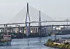 Große Schrägseilbrücke über einem Fluss mit Uferanlagen und Gebäuden im Hintergrund.