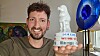 Fabian Kahl hält einen Mampe-Porzellanpudel in einem Raum mit Kunst und blauer Lampe.