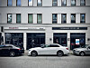 Pizzeria, Coffee Lab und geparkte Autos vor einer Gebäudefassade.