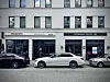 Pizzeria, Coffee Lab und geparkte Autos vor einer Gebäudefassade.