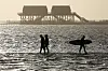 Surfer und Spaziergänger am Strand St. Peter-Ording mit Blick auf Stelzenbauten.