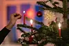 Jemand zündet eine rote Kerze an einem Weihnachtsbaum an.