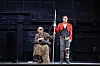 Theaterbühne. Links ein Mann im Rollstuhl und mit Sonnenbrille, rechts ein Mann mit verbundenem Bein. Sie halten sich an einer Stange fest