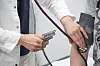 Arzt misst in einer Praxis den Blutdruck einer Patientin am Arm.