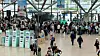 Reisende gehen durch eine große Abfertigungshalle am Flughafen Hamburg mit Anzeigen und Automaten.