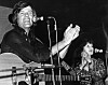Dean Reed singt 1976 in Westberlin mit Gitarre am Mikrofon, im Hintergrund eine Musikerin.