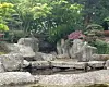 Steingarten mit Felsen, Wasserlauf und blühenden Sträuchern in einem grünen Park.