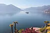 Lago Maggiore in der Schweiz mit Bergen, ruhigem Wasser und Uferbewuchs im Vordergrund.