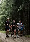 Mehrere Läufer (darunter HSV-Profi Noah Katterbach) auf einem Schotterweg im Wald, eine Gruppe folgt im Hintergrund.