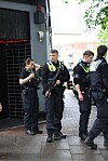 Mehrere Polizeikräfte stehen vor einem Gebäude auf nassem Gehweg.
