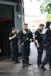Mehrere Polizeikräfte stehen vor einem Gebäude auf nassem Gehweg.