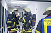 Feuerwehrleute rüsten sich im Krankenhausflur für eine Übung, ein Kollege schaut zu.