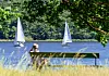 Frau auf Gartenbank beobachtet zwei Segelboote auf der Havel bei Sonne.