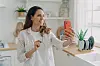 Junge Frau filmt sich mit Smartphone in heller Wohnküche.