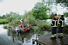 Feuerwehrkräfte am Ufer neben Einsatzboot und umgestürztem Baum im Wasser.