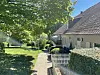 Gepflasterter Gartenweg neben Haus, Bäume links, weißer Zaun und Hecken rechts.