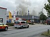 Feuerwehrfahrzeuge vor einem Gewerbegebäude, im Hintergrund dichter Rauch und abgesperrte Straße.