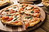Tiefkühlpizza mit Gemüse auf Holzbrett, in Stücke geschnitten, auf einem rustikalen Tisch.