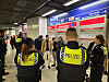 Polizeikräfte in gelben Westen stehen in einer Bahnhofshalle vor Anzeigetafeln und sprechen mit den Verdächtigen.