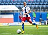 Fußballspieler läuft mit dem Ball auf dem Rasen vor leeren Stadionrängen.