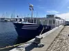 Blaue Segelyacht an der Hafenmole vor modernem Hafengebäude im Hafen