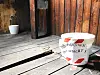 Weißer Becher mit handgeschriebenem Hinweis steht vor einer alten Holztür auf Holzboden.