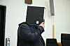 Mann im dunklen Anzug hält einen schwarzen Aktenordner vor das Gesicht im Gerichtssaal.