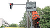 Arbeiter in Warnkleidung montiert ein Schild „Videokontrollen Parken“ an einer Ampel.