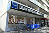 Budni-Logo an einer Hausfassade eines Drogeriemarkts mit Fahrrädern vor dem Eingang.