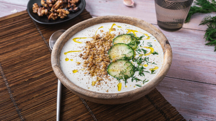 Schale kalter Gurkensuppe mit Gurkenscheiben, Kräutern und Gewürzen auf dem Tisch.