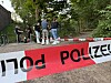 Polizeiband sperrt eine Straße ab, dahinter stehen Einsatzkräfte und Anwohner im Wohngebiet.