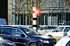 Blitzersäule mit rotem Warnlicht an einer Straße in Hamburg, umgeben von Autos und Gebäuden.