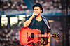 Musiker mit Hut singt und spielt Gitarre auf der Bühne vor Publikum.