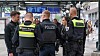 Polizeikräfte stehen in einer Bahnhofshalle vor Anzeigetafeln und sprechen mit einem Mann.